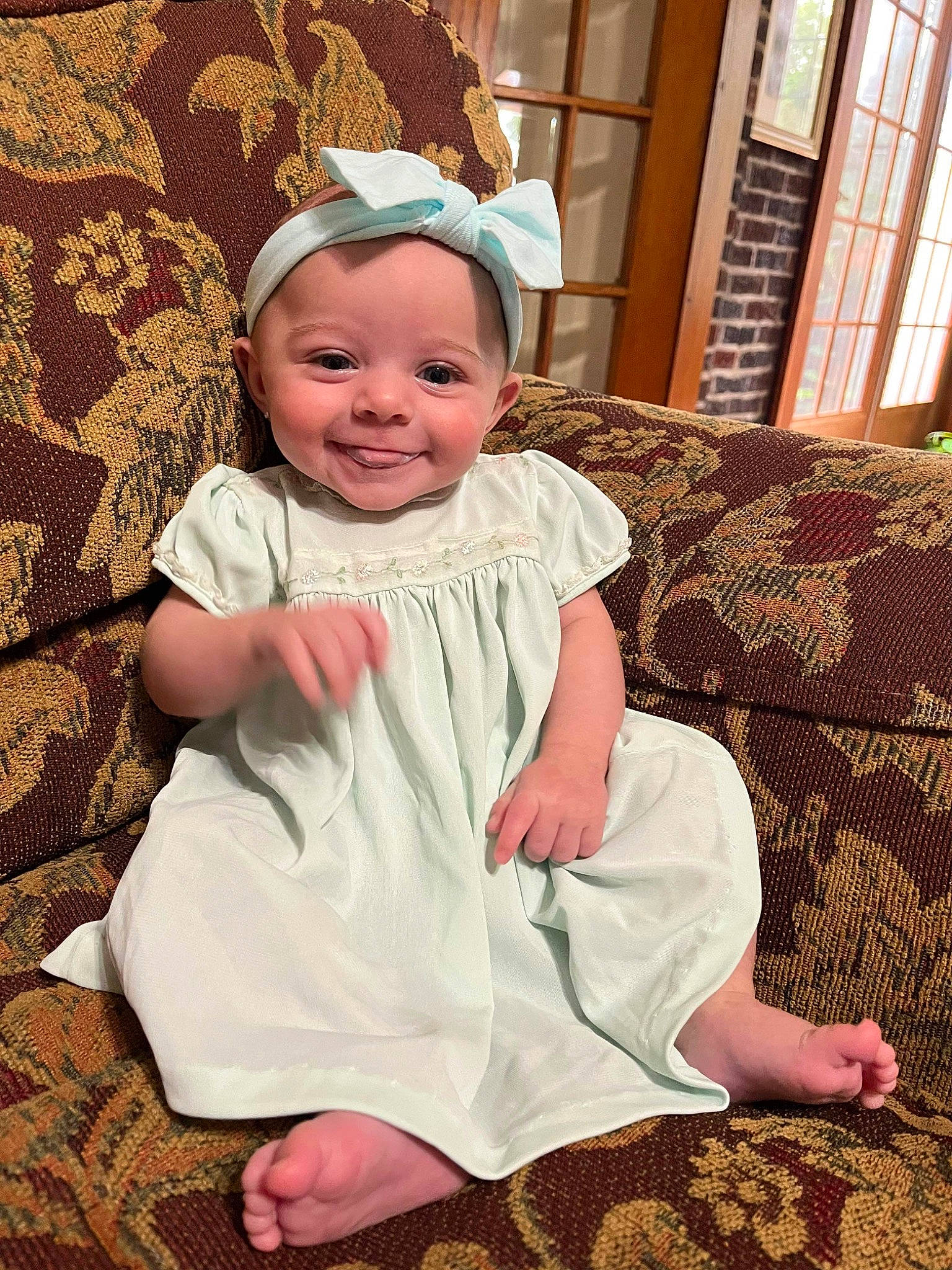 Quinn is registered to the contest to win money with this photo: baby, baby_toddler_clothing, child, comfort, couch, dress, event, face, flooring, fun, happy, head, joy, pattern, person, pink, sitting, skin, sleeve, smile