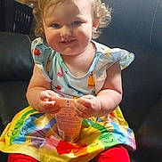 Violet is registered to the contest to win money with this photo: toddler, child, baby, sitting, smiling, portrait, indoor, armchair, snack, cup, food, dress, skirt, red_leggings, colorful_clothing, smiley_faces, blonde_hair, curly_hair, sunlight, happy