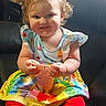 toddler, child, baby, sitting, smiling, portrait, indoor, armchair, snack, cup, food, dress, skirt, red_leggings, colorful_clothing, smiley_faces, blonde_hair, curly_hair, sunlight, happy