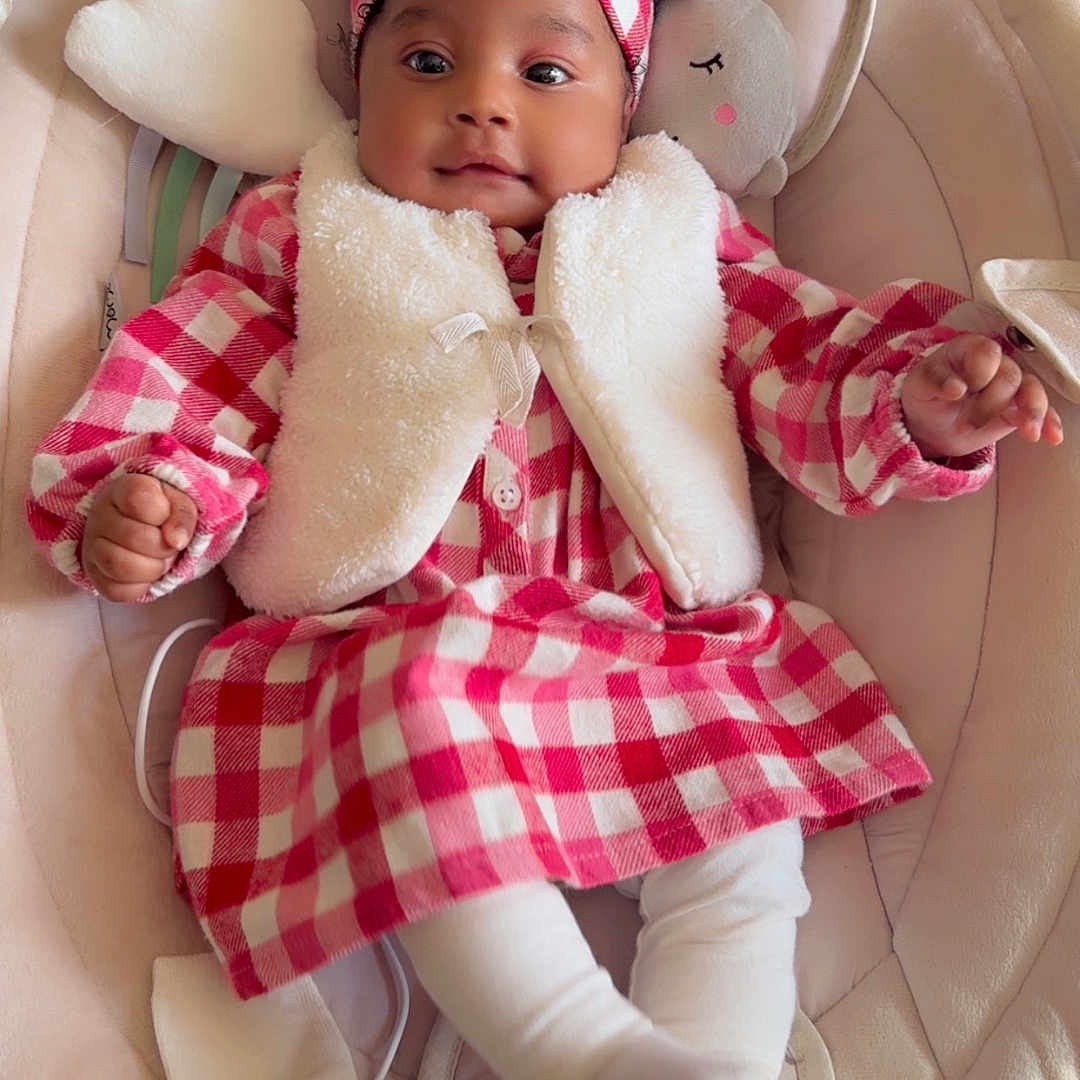 Soëlya a rejoint le concours — aidez-le/la à gagner de superbes lots ! baby, baby_rocker, checkered_pattern, child, clothing, comfort, cozy, cute, dress, happy, headband, indoor, infant, plush_toy, portrait, sitting, smiling, soft_fabric, toddler, white_vest