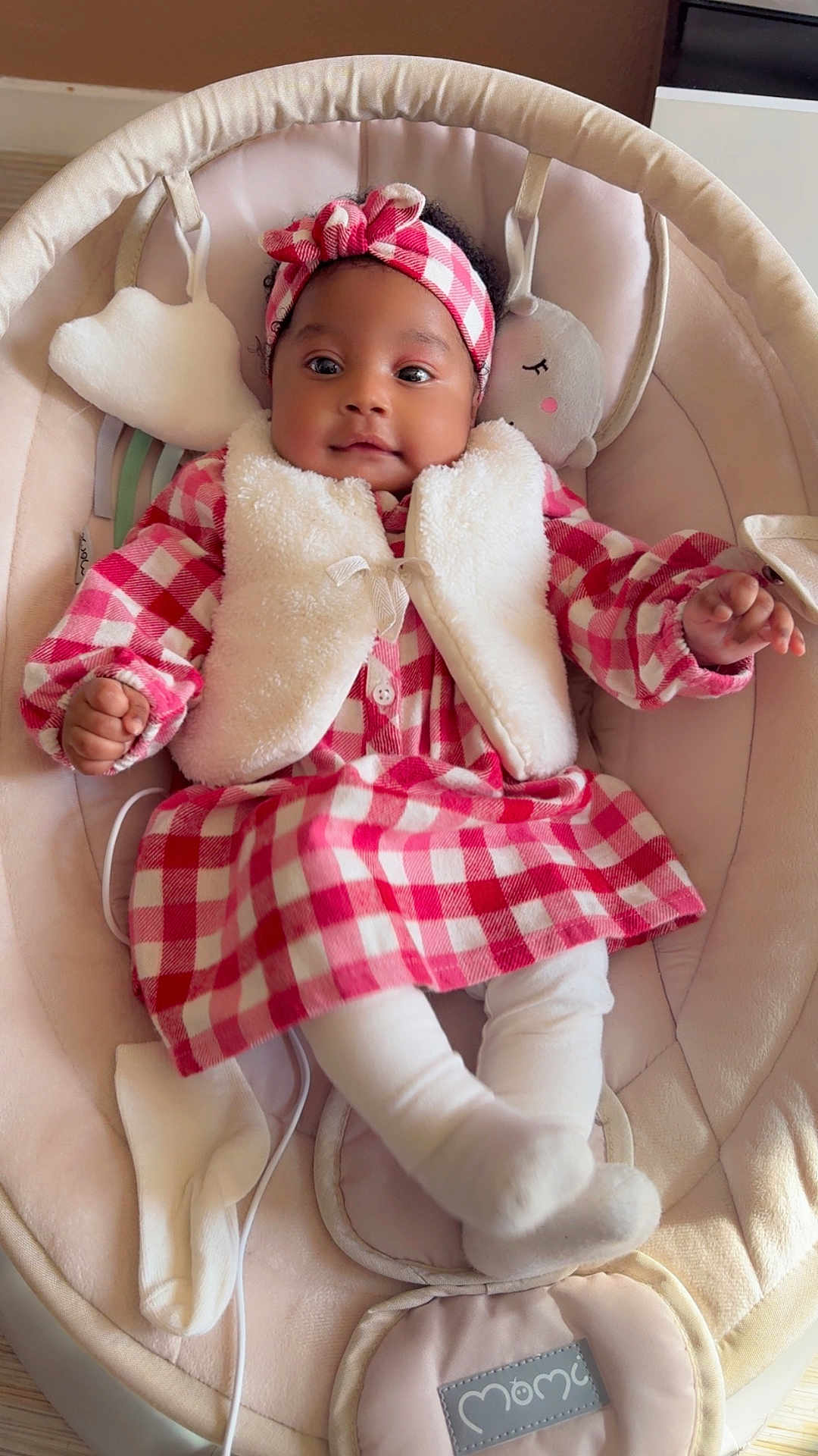 Soëlya a rejoint le concours — aidez-le/la à gagner de superbes lots ! baby, infant, child, dress, headband, plush_toy, baby_rocker, white_vest, checkered_pattern, cozy, smiling, cute, indoor, soft_fabric, toddler, sitting, clothing, comfort, portrait, happy