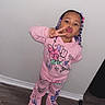 braided_hair, cartoon_clothing, child, flash_photography, furniture, girl, hair_beads, home, indoors, kissy_face, peace_sign, pink_pajamas, playful, portrait, smiling, sneakers, standing, toddler, wall, wooden_floor