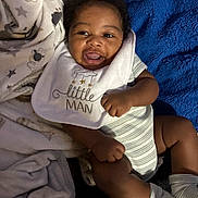 Tavon Jr joined the competition — help win amazing prizes! baby, infant, child, smiling, portrait, lying_down, bib, onesie, blanket, cozy, indoor, bed, blue_blanket, striped_clothing, socks, dark_skin, happy, face, baby_clothing, photograph