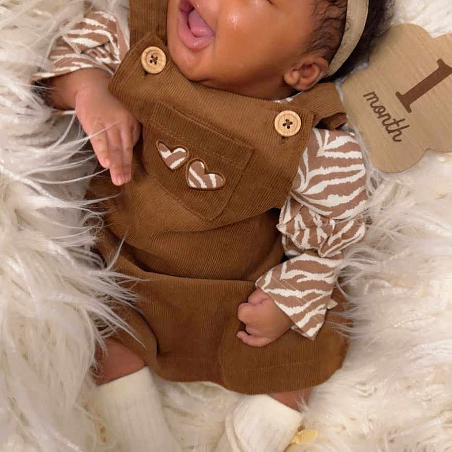 Zalayah Eaton is registered to the contest to win money with this photo: baby, infant, child, portrait, smiling, tongue_out, headband, flower, overalls, brown_clothing, striped_sleeves, socks, blanket, fluffy_blanket, lying_down, indoor, cozy, happy, close_up, photography