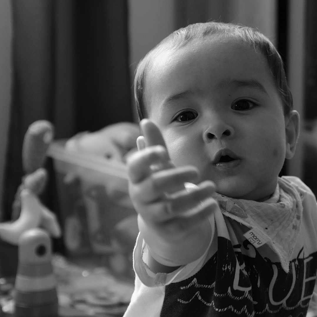 Liam a rejoint le concours — aidez-le/la à gagner de superbes lots ! baby, bandana, black_and_white, blurred_background, child, closeup, clothing, curious, expression, face, furniture, hand, home, indoors, person, playroom, portrait, toddler, toy, young_child