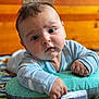 Brody is registered to the contest to win money with this photo: baby, infant, child, cute, face, eyes, onesie, pillow, blanket, hand, fist, wooden_background, indoors, portrait, closeup, expression, soft_toys, colorful, lying_down, curious
