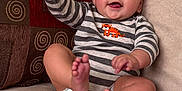 Brody is registered to the contest to win money with this photo: baby, child, smiling, striped_onesie, tiger_patch, couch, beige, pillow, spiral_pattern, happy, sitting, barefoot, indoor, cute, infant, expression, waving, cheerful, portrait, cozy