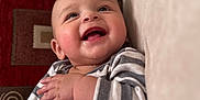 Brody is registered to the contest to win money with this photo: baby, smiling, drool, striped_clothing, couch, cushion, face, infant, happy, chubby_cheeks, indoors, person, young_child, seated, cozy, portrait, hand, skin, head, cute