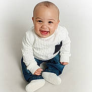 Honor is registered to the contest to win money with this photo: baby, blue_jeans, casual_clothing, child, cute, front_view, happy, indoors, infant, isolated, person, portrait, sitting, small_child, smiling, studio, white_background, white_shoes, white_sweater, young_child