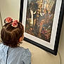 artwork, back_view, blue_striped_shirt, chair, child, curiosity, decor, elephant, framed_picture, hair, hair_accessory, indoor, lighting, pink_flower, portrait, reflection, room, soft_focus, toddler, wall