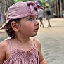 baby, blurry_background, casual, child, curious, cute, daytime, hat, outdoor, person, pink_cap, pink_dress, portrait, side_profile, street, summer_clothing, toddler, urban, walking_people, young_child