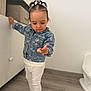 toddler, child, denim_jacket, white_leggings, sneakers, indoor, cabinet, wooden_floor, curious, hair_style, mini_pigtails, white_wall, flooring, footwear, person, standing, leaning, casual_clothing, young_child, exploring