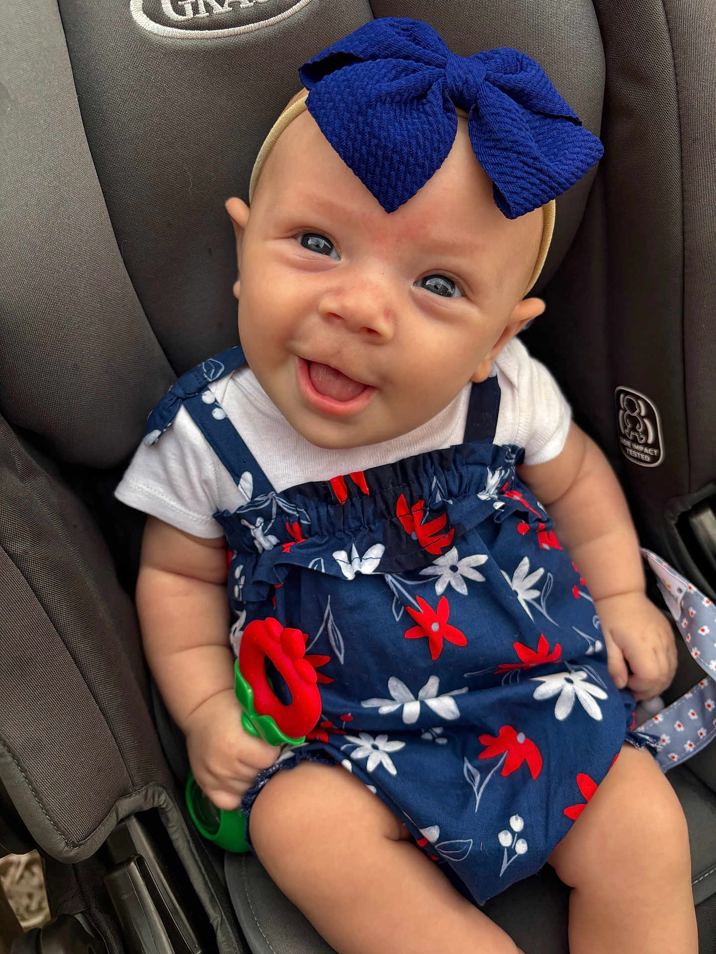 Madilynn joined the competition — help win amazing prizes! baby, child, smile, blue_bow, floral_dress, car_seat, toy, happy, cute, infant, portrait, sitting, clothing, red_flower, white_shirt, headband, hand, legs, face, closeup