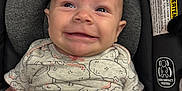 Madilynn is registered to the contest to win money with this photo: baby, infant, smile, car_seat, blanket, onesie, patterned_clothing, face, head, skin, arm, child, happy, expression, seat, safety, indoors, closeup, young, person