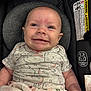 baby, infant, smile, car_seat, blanket, onesie, patterned_clothing, face, head, skin, arm, child, happy, expression, seat, safety, indoors, closeup, young, person