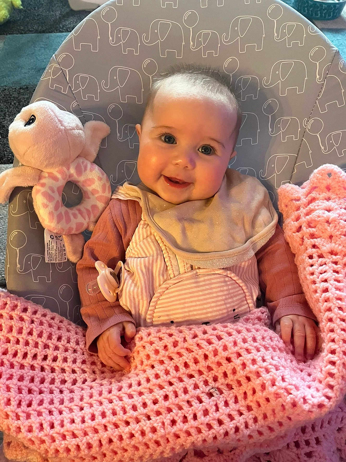 Penelope is registered to the contest to win money with this photo: baby, smiling, blanket, crochet, plush_toy, octopus_toy, baby_bib, pacifier, baby_clothing, baby_chair, elephant_pattern, indoor, child, happy, cute, portrait, infant, pink, beige, cozy