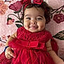 baby, child, smile, red_dress, bow, headband, dimples, tongue, floral_blanket, cute, portrait, infant, happy, indoors, person, lace, tulle, hand, face, soft