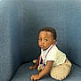 award, baby, blue_chair, candid, casual_clothing, child, curious, cute, fuzzy_pants, indoor, looking_away, medal, person, plush, portrait, sitting, small_hands, soft_texture, toddler, young_child
