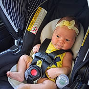 Octavia is registered to the contest to win money with this photo: baby, infant, car_seat, yellow_outfit, headband, baby_bottle, straps, safety, drool, cute, child, seat_belt, black, white, striped, comfort, alert, inside, closeup, person