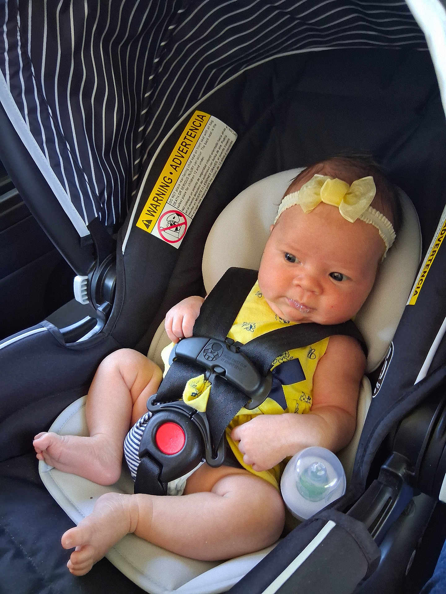 Octavia is registered to the contest to win money with this photo: baby, infant, car_seat, yellow_outfit, headband, baby_bottle, straps, safety, drool, cute, child, seat_belt, black, white, striped, comfort, alert, inside, closeup, person