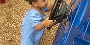 Zylah Brown is registered to the contest to win money with this photo: toddler, child, playground, steering_wheel, blue_play_structure, wood_chips, grass, outdoor, curly_hair, hair_ties, playing, side_view, casual_clothing, short_sleeves, imaginative_play, young_child, daylight, park, fun, active