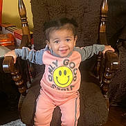Zylah Brown joined the competition — help win amazing prizes! child, toddler, smiling, pink_clothing, gray_clothing, tracksuit, sneakers, rocking_chair, wooden_furniture, brown_cushion, carpet, indoor, happy, person, home, floor, hair, sitting, arms_outstretched, face