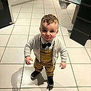Naym a rejoint le concours — aidez-le/la à gagner de superbes lots ! toddler, child, boy, curly_hair, bow_tie, overalls, cardigan, black_shoes, indoor, kitchen, tile_floor, standing, smile, portrait, young_child, fashion, cute, person, clothing, shadow