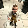 toddler, child, boy, curly_hair, bow_tie, overalls, cardigan, black_shoes, indoor, kitchen, tile_floor, standing, smile, portrait, young_child, fashion, cute, person, clothing, shadow