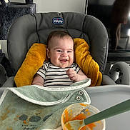 Paul participe au concours pour gagner de l'argent avec cette photo : baby, baby_food, bib, child, container, cushion, cute, feeding, feeding_time, furniture, happy, high_chair, indoor, messy, orange_food, person, smiling, spoon, striped_shirt, television