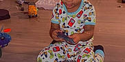 Jamir is registered to the contest to win money with this photo: toddler, child, pajamas, toy, floor, play_mat, indoor, game_controller_prints, sitting, playing, wooden_floor, colorful_clothing, young_child, focus, casual, home, cute, small_toys, plastic_toy, checkered_pattern