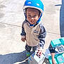 toddler, child, helmet, toy_car, outdoor, play_kitchen, concrete, shadow, jacket, sneakers, blue, curious, standing, daylight, play, person, cute, looking_up, casual_clothing, young_child