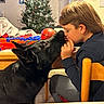 Cairo is registered to the contest to win money with this photo: boy, dog, black_dog, child, indoor, christmas_tree, holiday, table, chair, toys, basketball, nuzzle, love, warmth, home, portrait, furniture, casual_clothing, cute, family