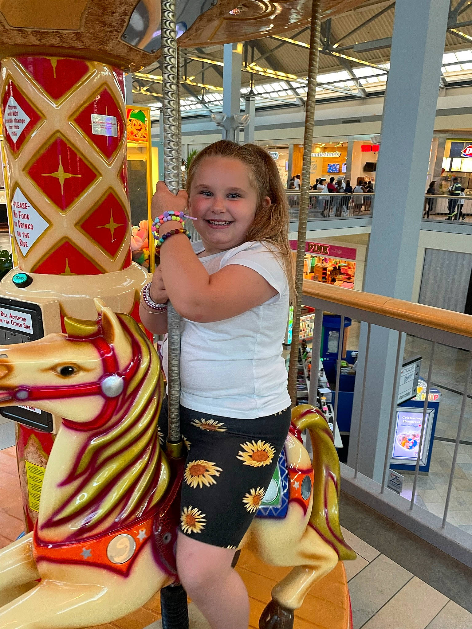 Ellie is registered to the contest to win money with this photo: amusement_park, amusement_ride, carousel, child, event, fun, happy, human_leg, joy, leisure, nonbuilding_structure, person, playground, recreation, shorts, smile, snapshot, t_shirt, thigh, toddler