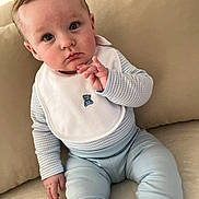 Myles is registered to the contest to win money with this photo: baby, child, infant, pajamas, bib, teddy_bear, couch, sofa, beige, blue, white, clothing, face, hand, expression, portrait, indoors, seated, person, cute