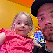 Myla a rejoint le concours — aidez-le/la à gagner de superbes lots ! child, girl, man, portrait, smile, pink_dress, beard, cap, indoor, arcade, colorful_background, happy, people, closeup, face, casual_clothing, yellow_wall, fun, family, together