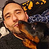Cora is registered to the contest to win money with this photo: man, dog, doberman, pet, close_up, face, affection, lick, blanket, indoors, cozy, friendship, love, expression, human, animal, portrait, warm, casual, relaxation