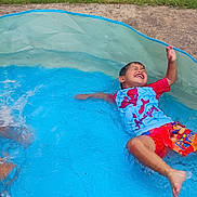 Mimi is registered to the contest to win money with this photo: child, swimming, pool, outdoor, summer, water, splashing, smiling, laughing, happy, playful, backyard, grass, swimwear, t_shirt, shorts, wet, recreation, family, portrait