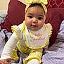 Divinity is registered to the contest to win money with this photo: baby, child, infant, yellow_clothing, headband, bib, smile, face, bed, blanket, pillow, indoors, cute, sitting, person, young_child, happy, portrait, clothing, fabric