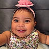 Divinity is registered to the contest to win money with this photo: baby, child, smiling, face, headband, flower, dress, sequin, sparkly, happy, cute, portrait, infant, young_child, person, indoors, cushion, gray_background, closeup, cheerful