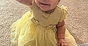 Divinity joined the competition — help win amazing prizes! baby, child, smiling, yellow_dress, headband, sitting, carpet, rug, sock, happy, indoors, person, footwear, patterned_rug, cute, infant, toddler, clothing, reaching, portrait
