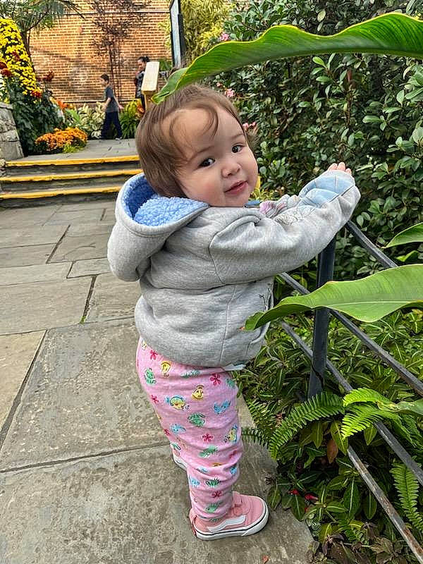 Annie is registered to the contest to win money with this photo: baby, baby_toddler_clothing, boot, child, flooring, fun, garden, grass, happy, leaf, leisure, people_in_nature, person, plant, sandal, sitting, smile, terrestrial_plant, toddler, tree