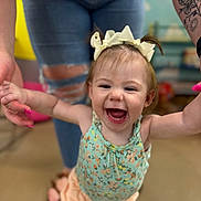 Alayna is registered to the contest to win money with this photo: toddler, child, smiling, happy, baby, bow, headband, person, adult, hand_holding, jeans, tattoo, flower_tattoo, ripped_jeans, indoor, floor, clothing, blurred_background, walking, support