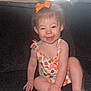 toddler, child, smiling, sitting, couch, orange_bow, floral_outfit, happy, indoors, baby, cute, person, young_child, skin, face, hand, foot, hair, furniture, portrait