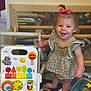Alayna is registered to the contest to win money with this photo: toddler, child, smiling, red_bow, green_dress, toy_walker, mirror, indoor, play_area, barefoot, colorful_toys, wooden_floor, happy, person, cute, young_child, standing, reflection, playtime, baby