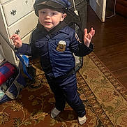 Riley joined the competition — help win amazing prizes! child, toddler, police_costume, blue_uniform, hat, indoor, rug, carpet, furniture, dresser, door, flooring, toy, bag, person, clothing, smiling, pose, home, play