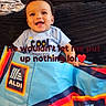 baby, child, smiling, couch, blanket, colorful, bag, indoor, text_overlay, happy, clothing, person, face, sitting, black_couch, red_rug, playful, cute, infant, home