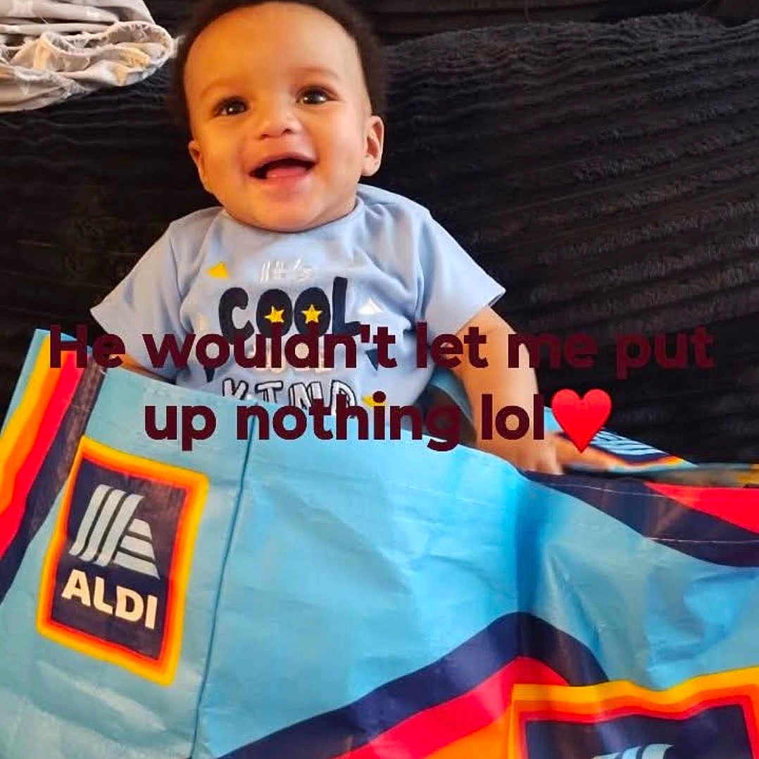 Messiah joined the competition — help win amazing prizes! baby, child, smiling, couch, blanket, colorful, bag, indoor, text_overlay, happy, clothing, person, face, sitting, black_couch, red_rug, playful, cute, infant, home