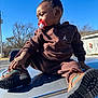 baby, blue_sky, boots, brown_tracksuit, car_roof, casual_wear, child, cute, daylight, expression, hairstyle, outdoor, pacifier, playful, portrait, sitting, sunny, toddler, topknot, trees