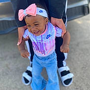 Ava is registered to the contest to win money with this photo: toddler, child, smiling, nike, headband, bow, adult_hands, jeans, outdoor, concrete, footwear, sandals, black_pants, colorful_clothing, baby, joyful, person, supporting, walking, fashion