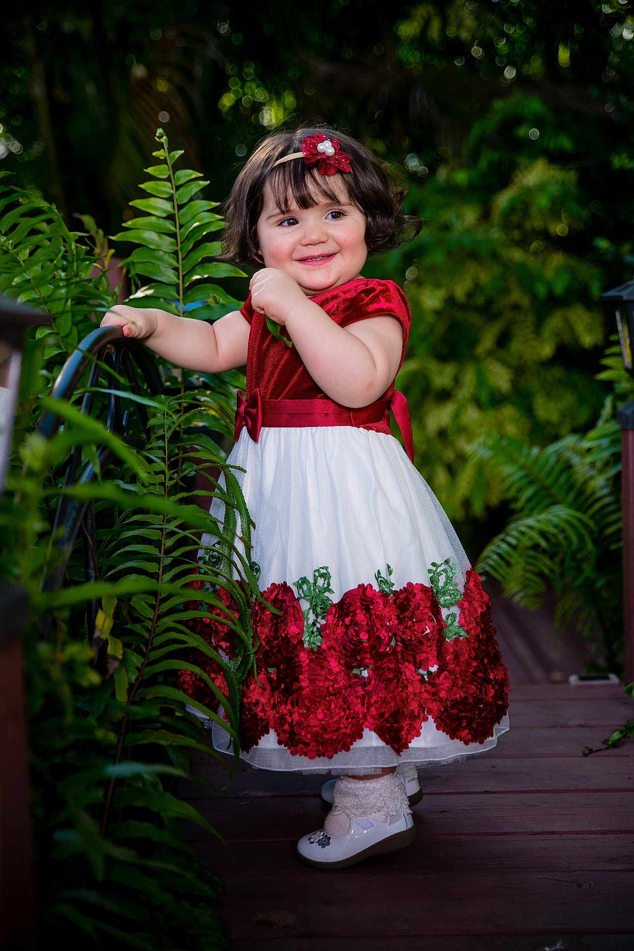 Vanessa joined the competition — help win amazing prizes! toddler, child, dress, red, white, flower, headband, smile, outdoor, nature, greenery, fern, portrait, cute, happy, footwear, socks, wooden_path, garden, person